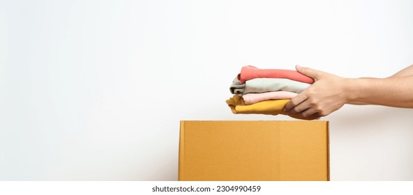 Donation, Charity, Volunteer, Giving, Delivery and Home Moving Concept. Hand holding Clothes into cardboard box at home for support and help poor, refugee and homeless people. Copy space for text - Powered by Shutterstock