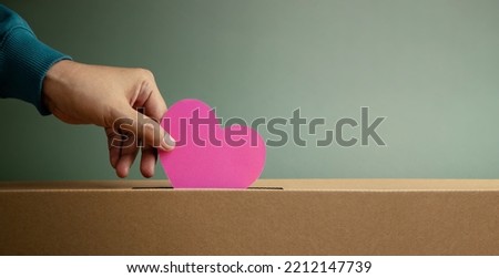 Donation Concept. Hand Droping a Pink Paper Heart into a Donate Box. Helping, Supporting and Togetherness. Side View