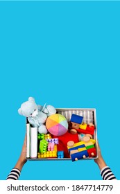 Donation Concept. Kid Hands With Donate Box With Clothes, Books And Toys On Light Blue Background. Top View