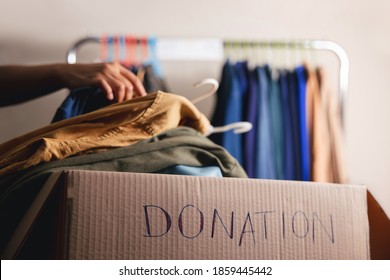 Donation Concept. Preparing Used Old Clothes From Wardrobe Rack Into A Donate Box. Focus On Text