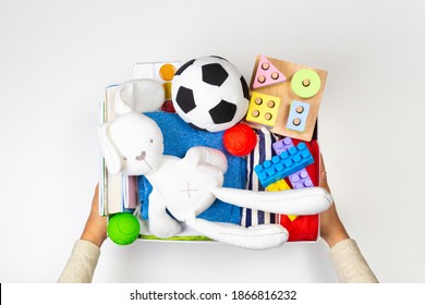 Donation Concept. Volunteer Hands Holding Donate Box With Clothes, Books And Toys On White Background. Top View