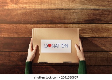 Donation Concept. Woman Givings A Box Of Things With Donate Label And Heart. Preparing On Wooden Table At Home. Top View