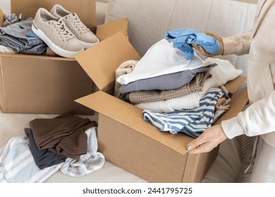 Donation concept. A woman puts clothes in a cardboard box at home for donation, recycling or disposal. Women's hands close up. - Powered by Shutterstock