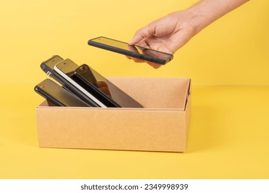 Donations of used cell phones. Hand put old cell phone to cardboard box full of used smartphones. Donation, e-waste, electronic waste charity, recycling concept - Shutterstock ID 2349998939