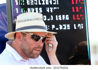 DONCASTER RACECOURSE, SOUTH YORKSHIRE, UK : 13 August 2022 : A Bookmaker Wearing A Panama Hat Adjusts His Sunglasses As He Stands In Front Of His Odds Board 