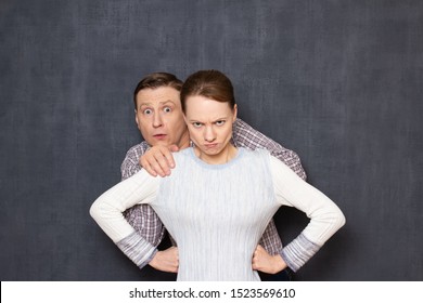Don't be afraid and don't worry, I defend you! Studio waist-up shot of brave fearless small woman protecting big scared man, hiding before her back, seeing something awful. Relationship concept