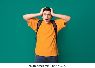 Don't believe. Surprised teen guy with hands on head over turquoise background