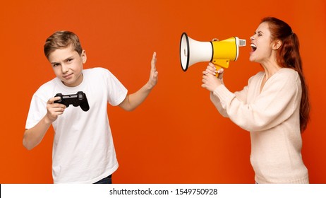 Don't Bother Me. Annoyed Teenager With Joystick Ignoring His Mom Talking To Him Through Loudspeaker, Orange Background