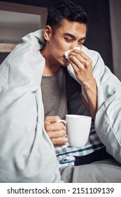 Dont Get The Flu, Get The Shot. Shot Of A Young Man Blowing His Nose And Having Tea While Recovering From An Illness In Bed At Home.