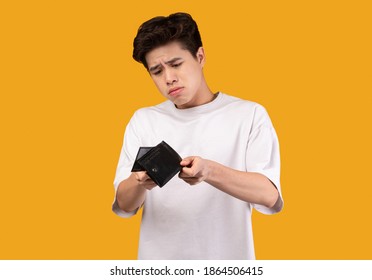 I Don't Have Money. Portrait Of Upset Asian Man Looking At His Empty Wallet. Depressed Sad Guy Standing Isolated Over Orange Studio Background Wall. Poverty, Financial Crisis And Bankruptcy Concept