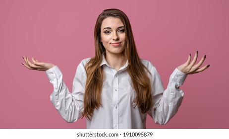 I dont know, its not me. Portrait of clueless and indecisive brunette girl shrugging with hands spread sideways, being confused, puzzled, pink background