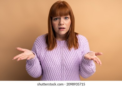 I Don't Know. Portrait Of Confused Beautiful Young Woman Standing With Raised Arms And Looking At Camera. Indoor Studio Shot Isolated On Orange Background 