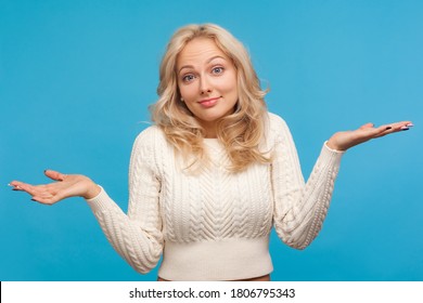 I dont know. Puzzled blond woman in white sweater shrugging shoulders, confused and uncertain with information. Indoor studio shot isolated on blue background