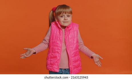 I Dont Know What To Say. Confused Girl Feeling Embarrassed About Ambiguous Question, Having Doubts, No Idea, Being Clueless And Uncertain. Young Little Child Isolated Alone On Orange Studio Background