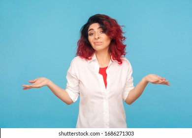 Don't know, whatever! Portrait of uncertain hipster woman with fancy red hair raising hands in helpless gesture, being careless indifferent to question. indoor studio shot isolated on blue background