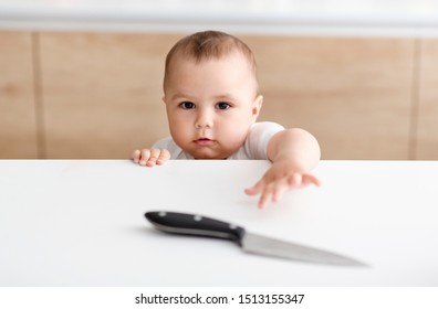 Don't Leave Kids Alone. Little Baby Boy Reaching Hand For Sharp Knife On Kitchen Table, Empty Space