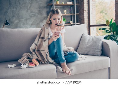 I don't love you anymore! Concept of problems in relationship. Disappointed young woman is eating tasty sugary donuts and looking old photos on her cellphone