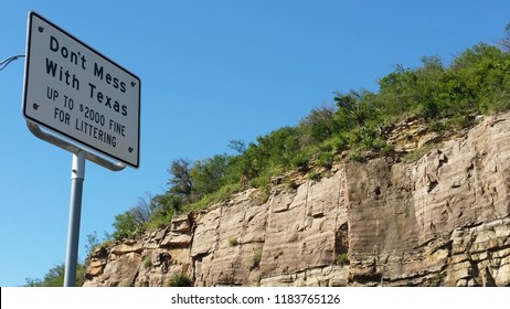 Don't Mess With Texas Sing By Road Cutting Hill With Rock Exposed And Green Trees And Grass On Top With A Clear Blue Sky