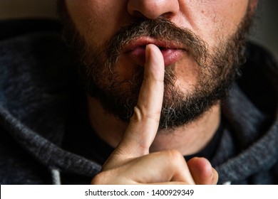 Don't speak, be quiet - close up portrait of bearded man on the door saying shhh. Finger on lips. Head and shoulders, no eyes. Danger. Violence concept.