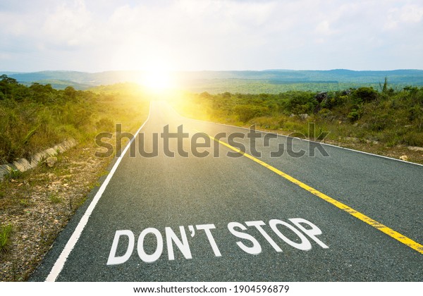 Don\'t stop\
inscription on straight road. Motivational inscription on the road\
going forward. The beginning of a new path. A conceptual photo of\
the path leading to a bright\
future.