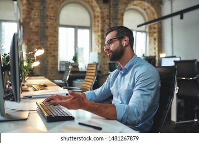 I don't understand. Side view of young and successful bearded man in eyeglasses and headphones typing something on computer and gesturing while sitting in the modern office - Shutterstock ID 1481267879