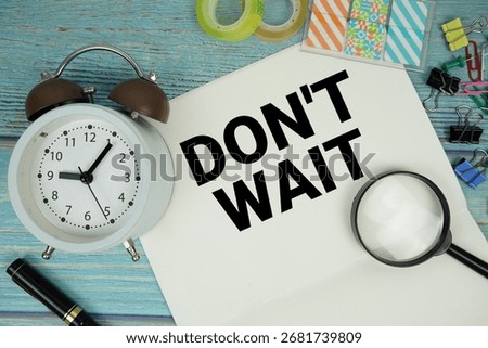 Don't Wait text written on notepad with alarm clock and magnifying glass flat lay on wooden background