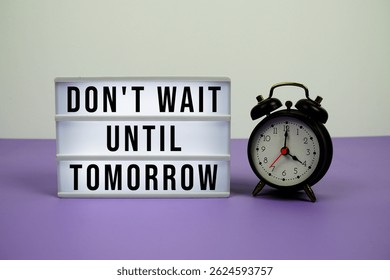 Don't Wait Until Tomorrow text on LED lightbox with alarm clock on purple background
