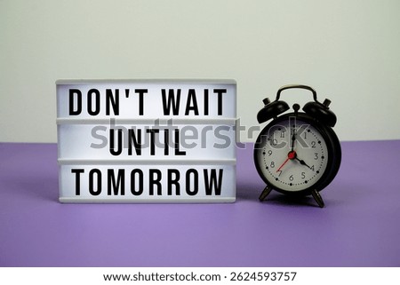 Don't Wait Until Tomorrow text on LED lightbox with alarm clock on purple background