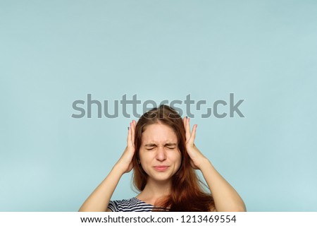 don't want to hear it. rejection refusal and denial. young woman covering ears with hands. portrait of a girl with tightly shut eyes on blue background.