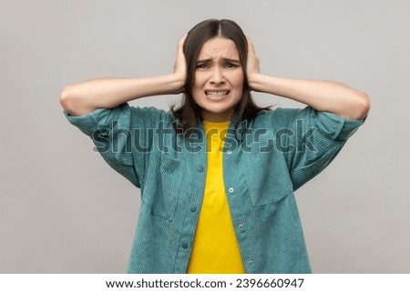 Don't want to listen anymore. Angry woman covering ears with hands to stop hear annoying talk, avoiding high-decibel sound, wearing casual style jacket. Indoor studio shot isolated on gray background.