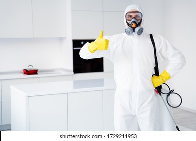 Dont worry we kill covid19. Serious successful cleaner worker guy in yellow gloves show thumb up sign approve spray decontamination stop spread disinfection wear latex gloves goggles in house kitchen - Shutterstock ID 1729211953