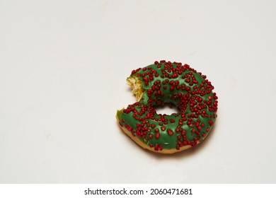 Donut close-up on white background. Donut bitten off isolated. Green donat wit red decorative candy