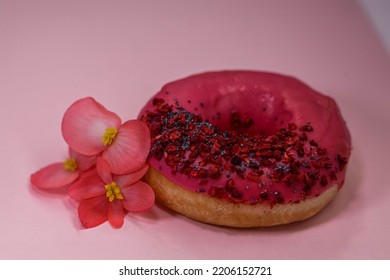 Donut With Pink Icing And Colored Sprinkles, Poppy Seeds And Dry Raspberry On Pink Background With Edible Rose Begonia Petals Flowers. Tasty Delicious Fat High Calories Sweet Food. Selective Focus