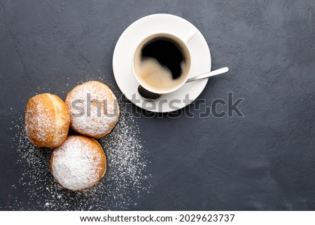 Donuts (buns) with powdered sugar and coffee for breakfast. Black background. Top view with copy space.