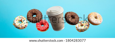 Donuts flying in the air and coffee paper cup on a blue background. Bakery, baking concept. Levitation. Banner