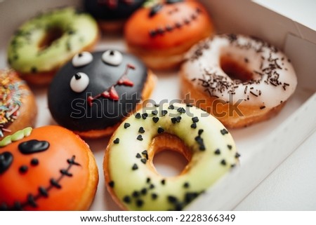 Donuts with Halloween decoration of monsters with spooky face and zombie by syringe with sugar syrup. Different colorful traditional sweets and doughnuts of hallows eve at autumn season indoor