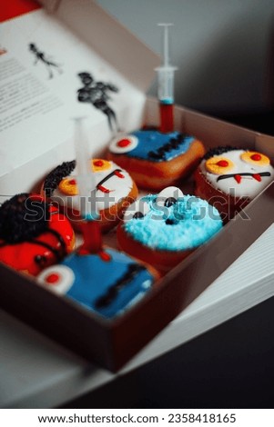 Donuts with Halloween decoration of monsters with spooky face and zombie by syringe with sugar syrup. Different colorful traditional sweets and doughnuts of all hallows eve at autumn season indoor