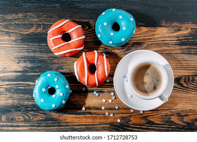 Donuts One With Blue Icing And White Stars And With Red Icing And White Stripes And A Cup Of Coffee On A Wooden Table