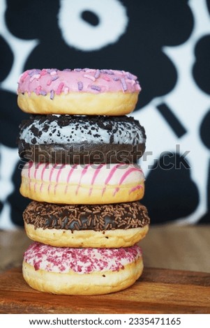 Donuts with pink and chocolate icing with sprinkles in a column on a wooden table                               