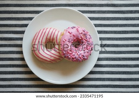  Donuts with pink icing on a white plate on a striped background                              