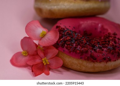 Donuts With Pink And Violet Icing And Colored Sprinkles With Poppy Seeds And Dry Raspberry On Pink Background With Pink Begonia Petals. Tasty Delicious Fat High Calories Sweet Food. Selective Focus