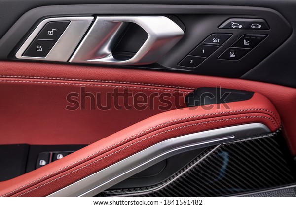 Сlose up of a\
door control panel  with chrome handle on the car door, common\
black and red genuine leather in a new car. Arm rest with  seat\
setting and open trunk  control\
panel
