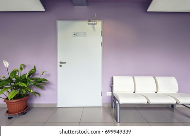 Door Of Doctor's Office In Clinic, Purple Interior With Chairs And Flower. Empty Light Hall, Corridor Of Modern Clinic Or Hospital. Theme Of Doctor Consulting, Health, Decor And Medicine.