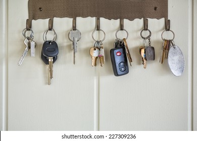 Door, house, and car keys hanging on hooks on a wall.