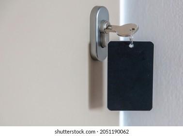 Door Key With Blank Label In The Keyhole. Steel Key Ring, Room Key And Empty Black Tag For Text Or Number Close Up View. House, Hotel Or Motel Room Open, Unlock Concept. Copy Space, Template