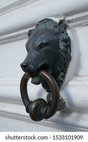 A Door Knocker In The Shape Of A Dog’s Head. On A White Door.