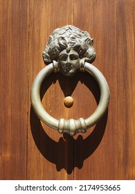 Door knocker in the shape of a woman's head, the knocker ring draws its shadow on the wooden door.
