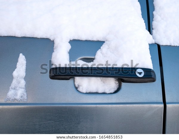 The door lock of the car in\
the snow close-up in winter. The door handle is covered with\
snow.