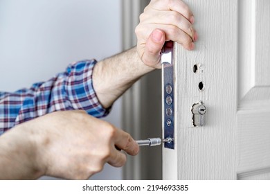 Door lock installation, repair, or replacement service. Door hardware installer locksmith working with open white door indoor. Hands of the master close-up