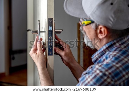 Door lock installation, repair, or replacement service. Door hardware installer locksmith working with open white door indoor.